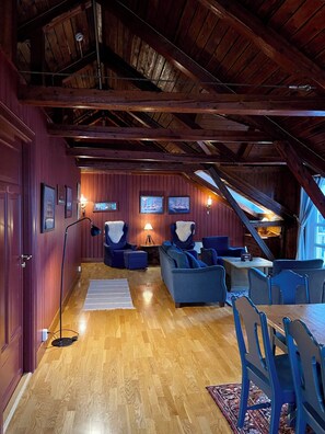 An attic-style room with wooden beams, a wooden floor, and a seating area with blue upholstered chairs and sofas.