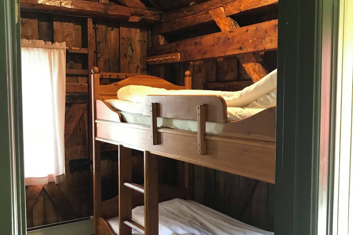 A bunk bed room with wooden walls and a window with a curtain.