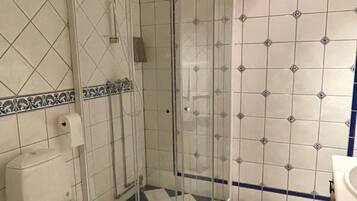 A bathroom with a white toilet, a glass-enclosed shower, and blue-tiled walls.