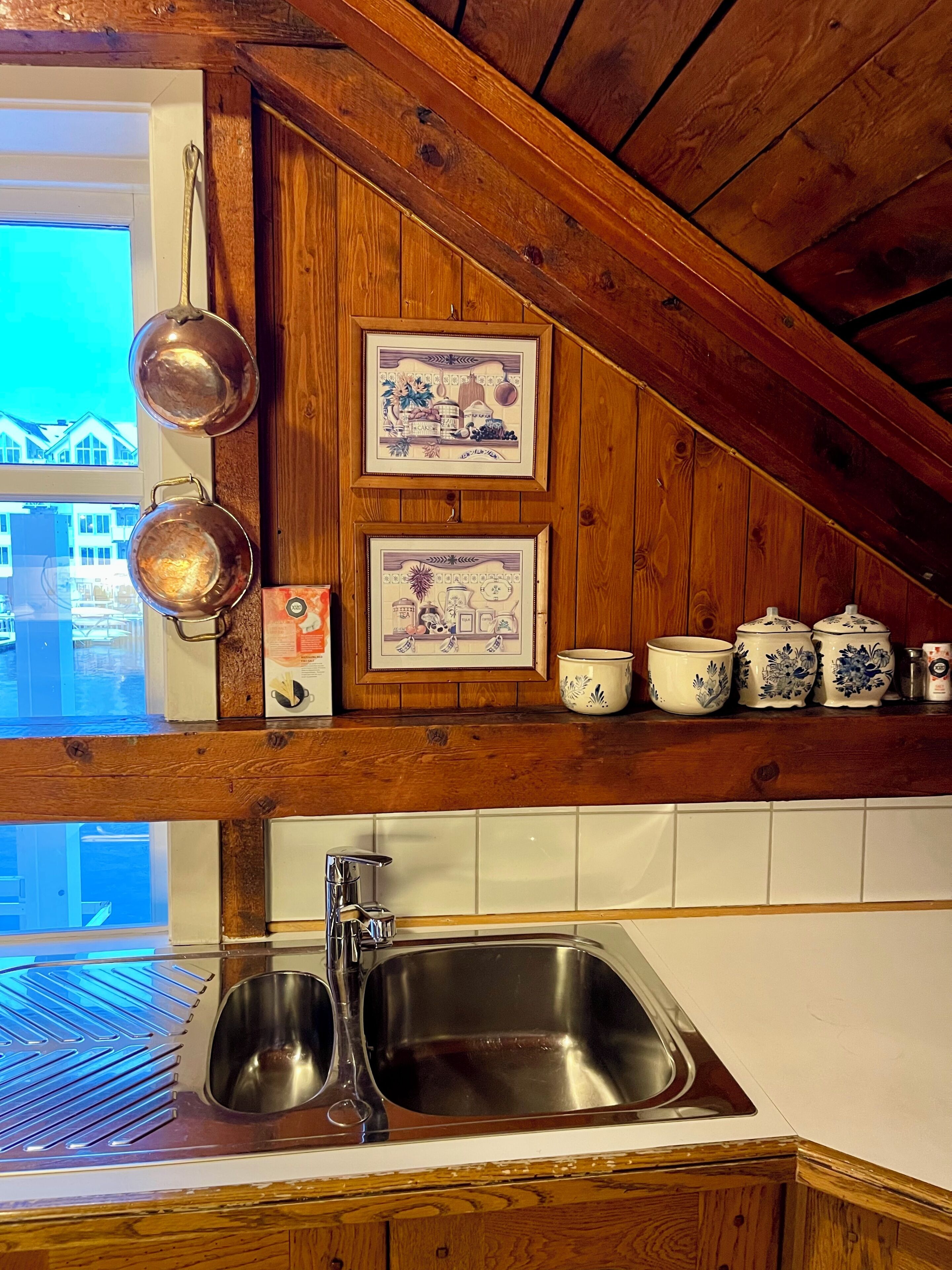 A kitchen with wooden beams, a stainless steel sink, and decorative items on the wall.