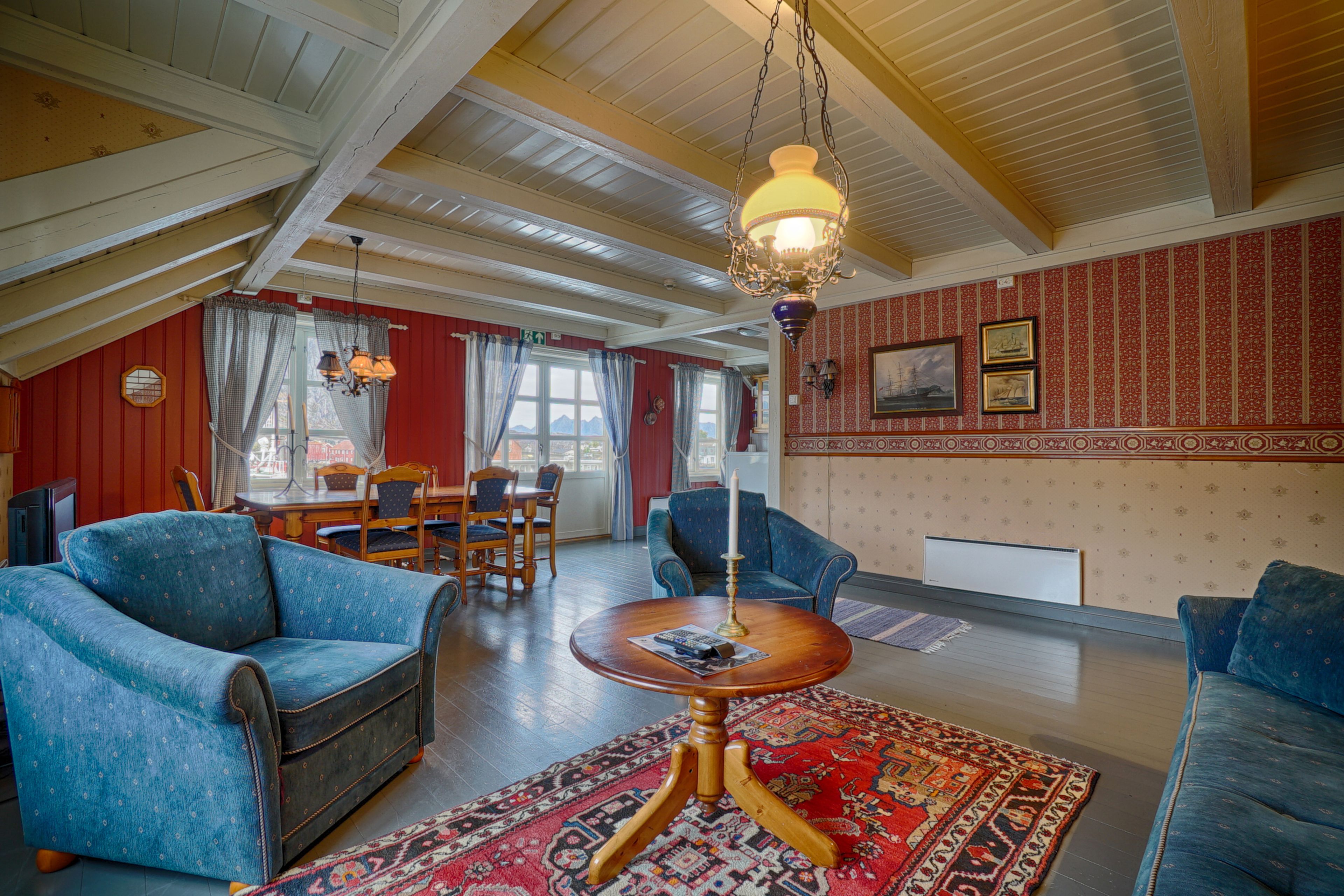 A spacious living room with high ceilings, a wooden ceiling, and a large window. There is a blue sofa, a wooden coffee table, and a patterned rug.