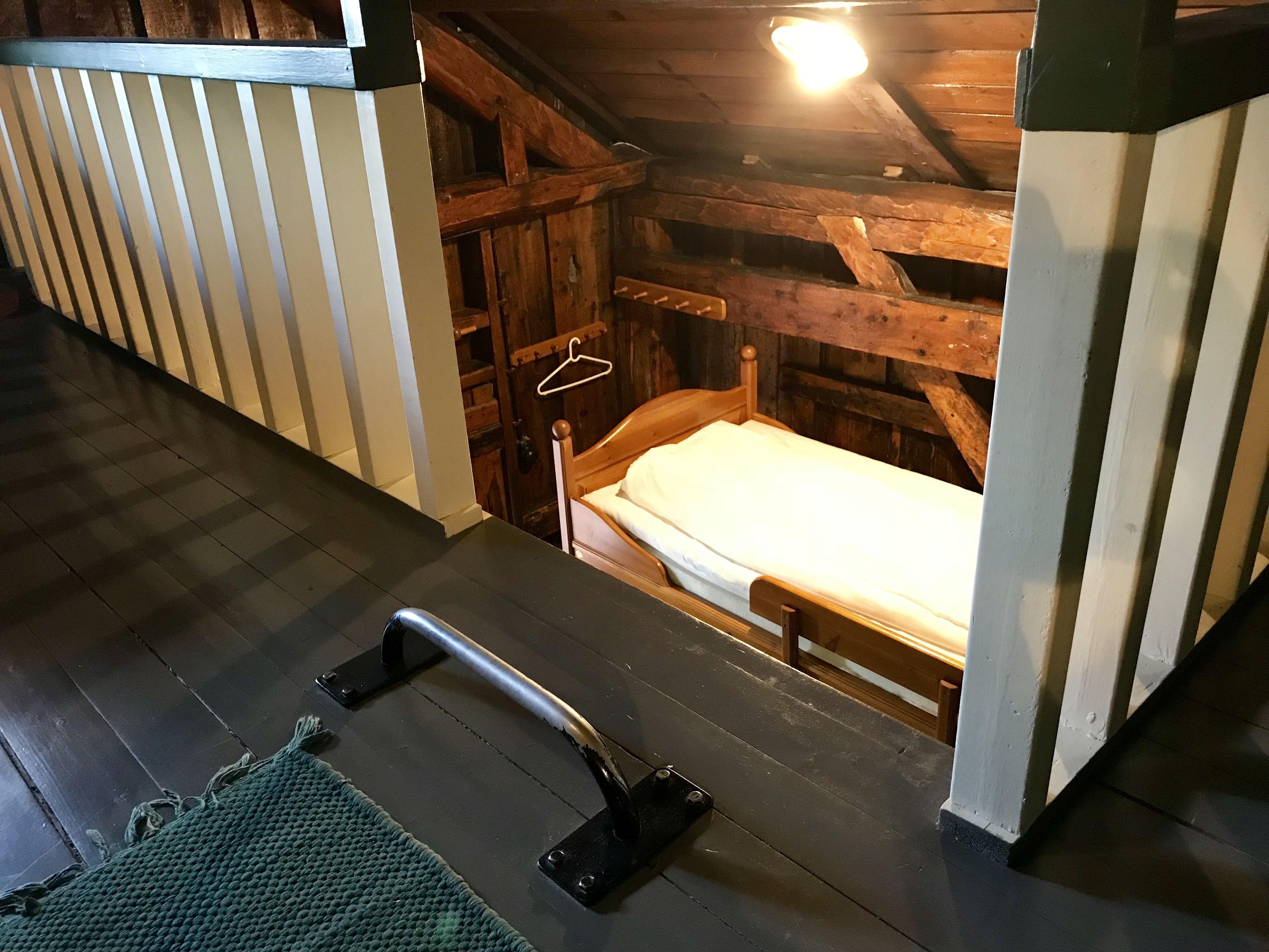 Une petite pièce rustique en bois, avec un lit simple, un banc en bois et un luminaire suspendu.