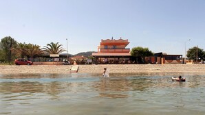 A building with a flat roof and a balcony, situated next to a body of water. - Ninos on the Beach (Corfu)