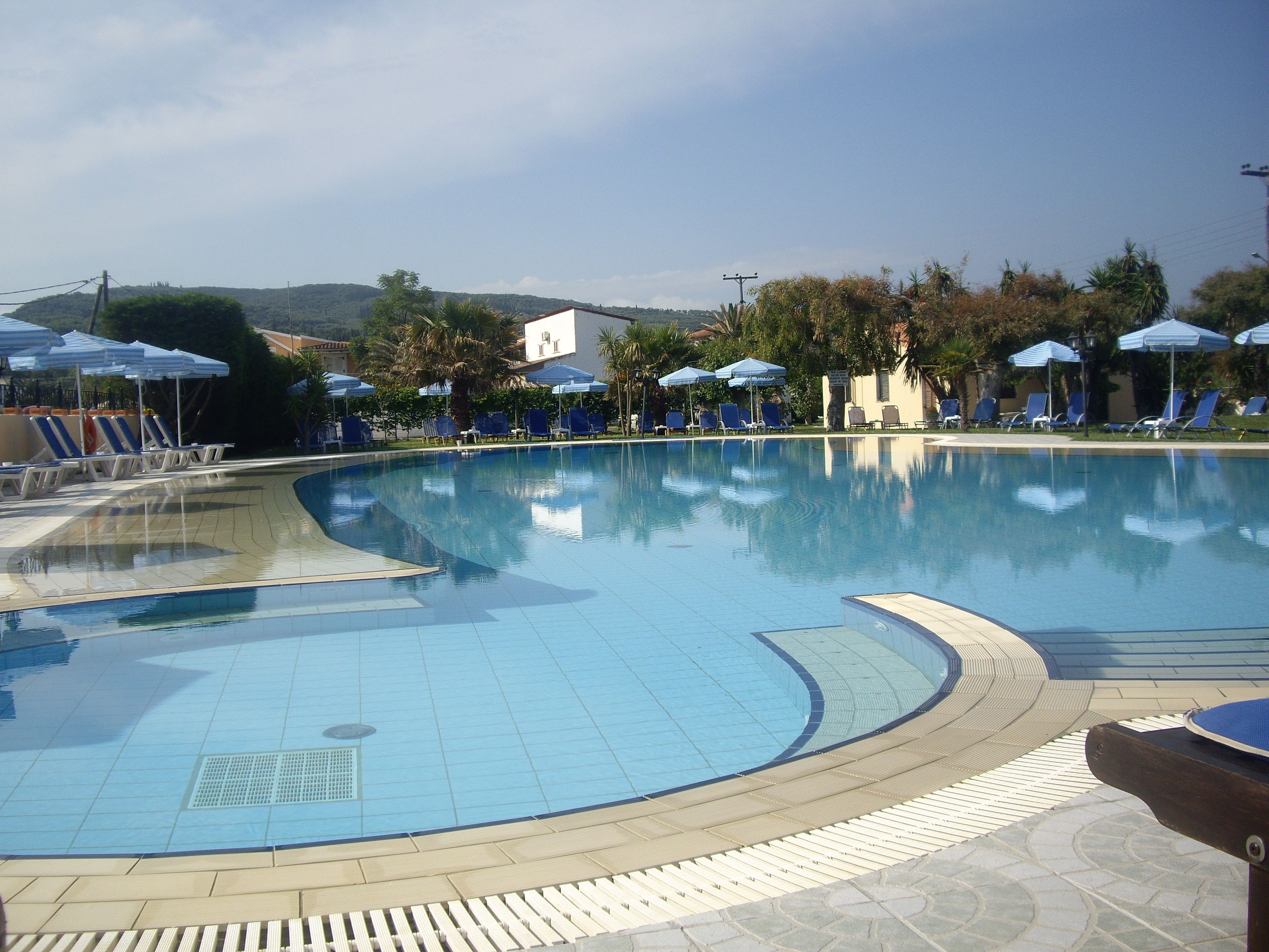 A swimming pool with blue tiles, surrounded by lounge chairs and umbrellas.