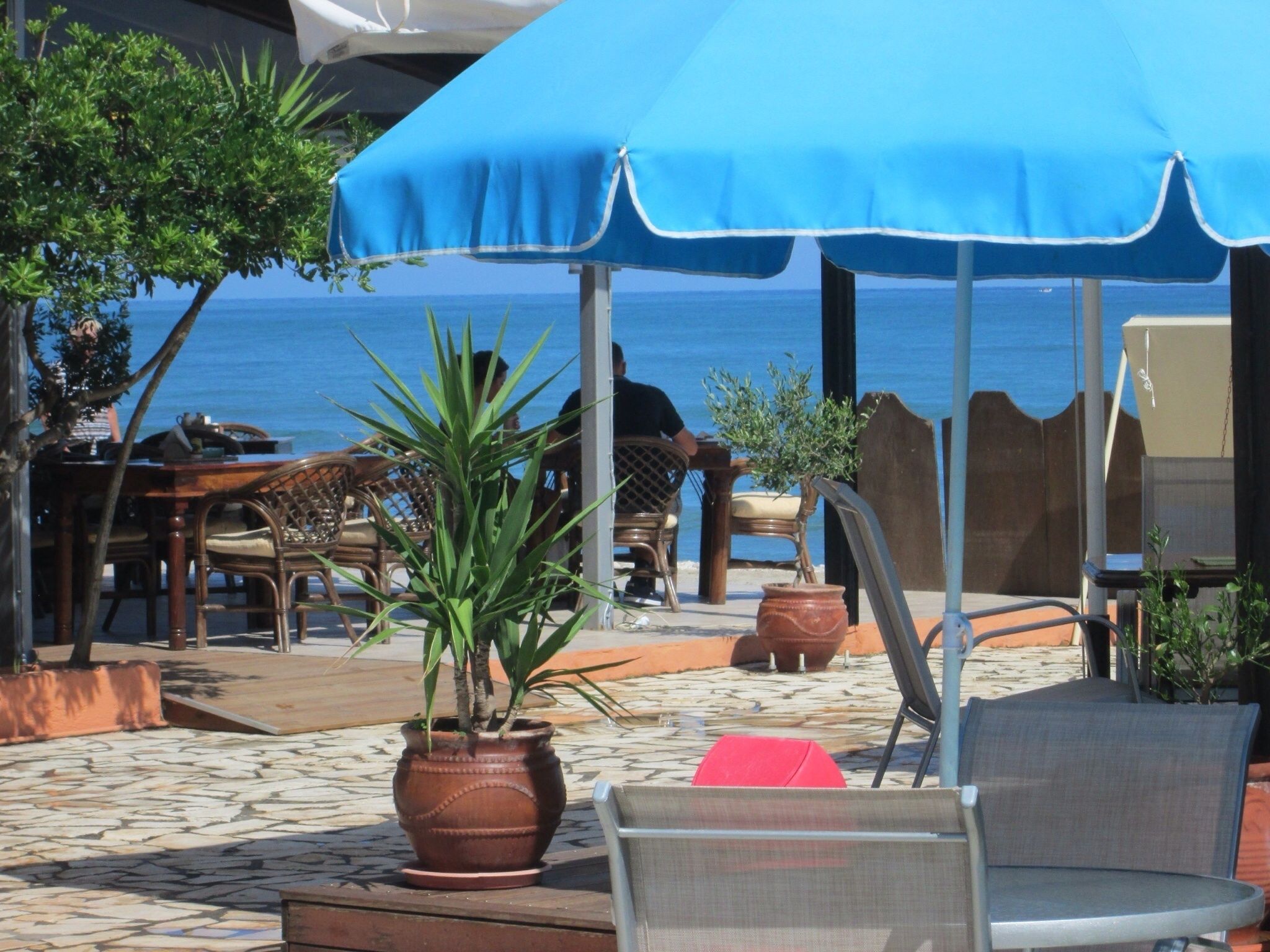 Un espace extérieur aménagé avec des sièges, un parasol bleu, des chaises en osier et un pot de fleurs.