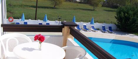 A poolside area with a view of a residential area, a table with chairs, and a flower vase.