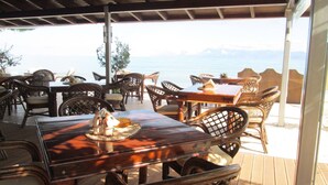 An outdoor dining area with wooden tables and chairs, overlooking a scenic view of the sea. - Ninos on the Beach (Corfu)