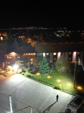 A hotel with a well-lit entrance, a parking area, and a person walking. - Hotel Picos del Sur (El Calafate)