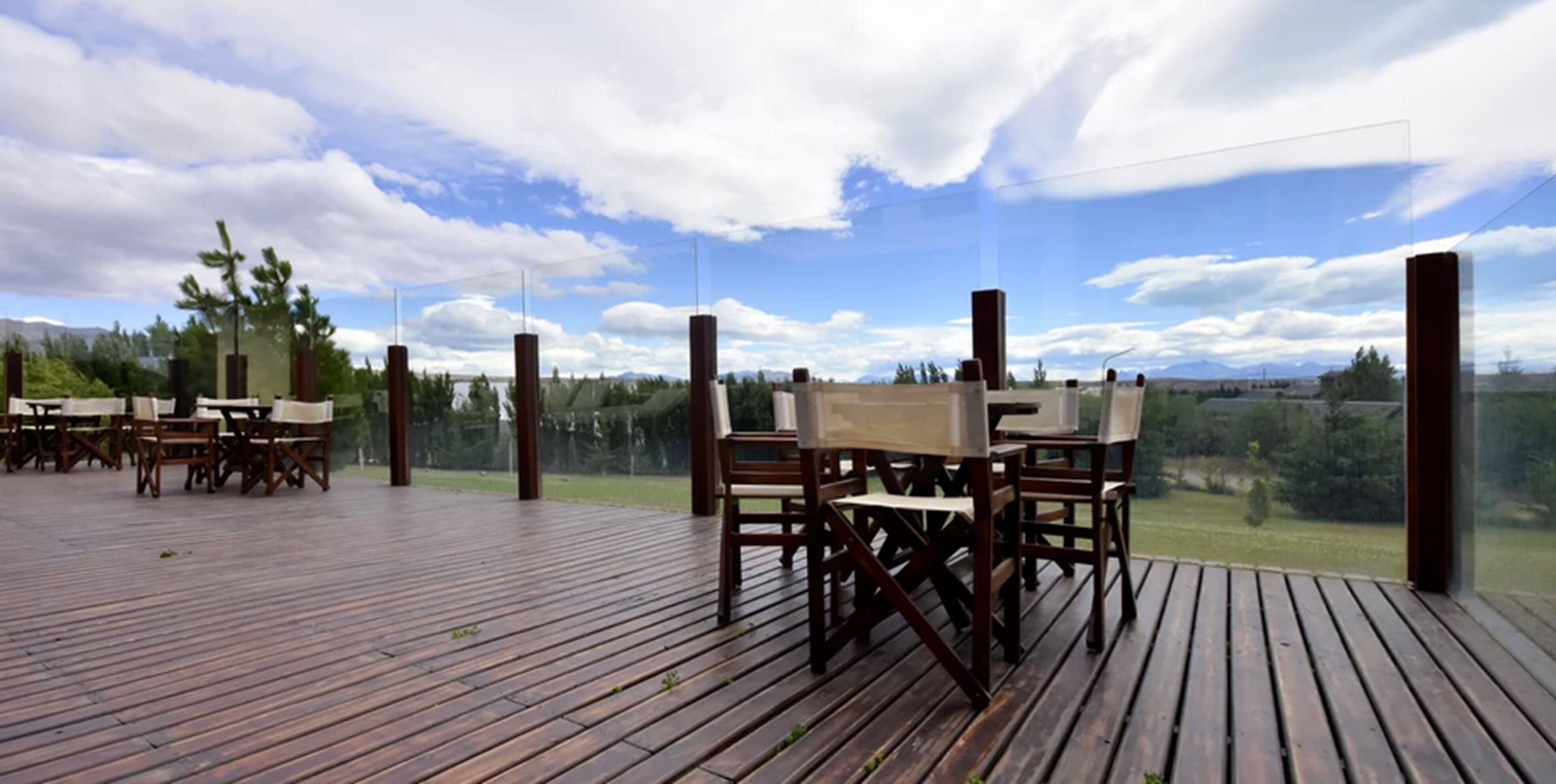 Una terraza de madera al aire libre con mesas y sillas, con vistas a un paisaje pintoresco con árboles y montañas.