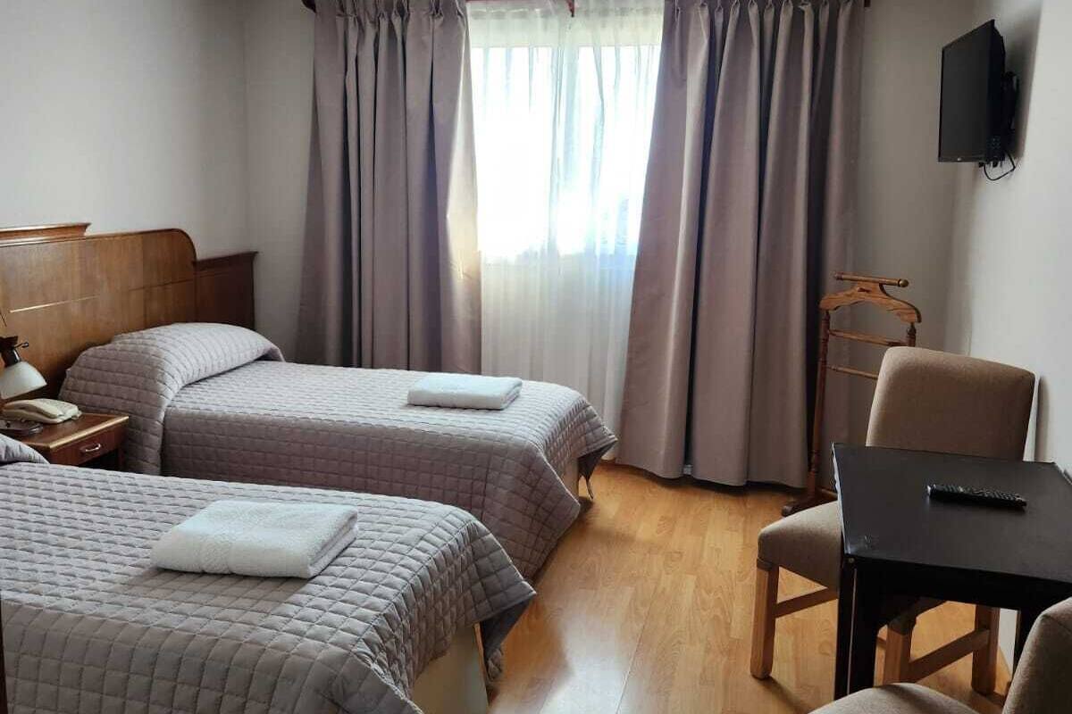 A hotel room with two beds, a desk, a chair, a TV, and a window with curtains.