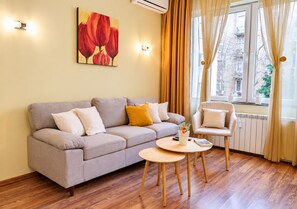 A living room with a sofa, a chair, a small table, and a window with curtains. - BIZ Apart Sofia (Sofia)