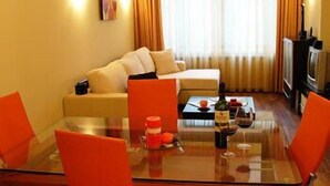 A living room with a glass dining table, orange chairs, a sofa, and a television. - BIZ Apart Sofia (Sofia)