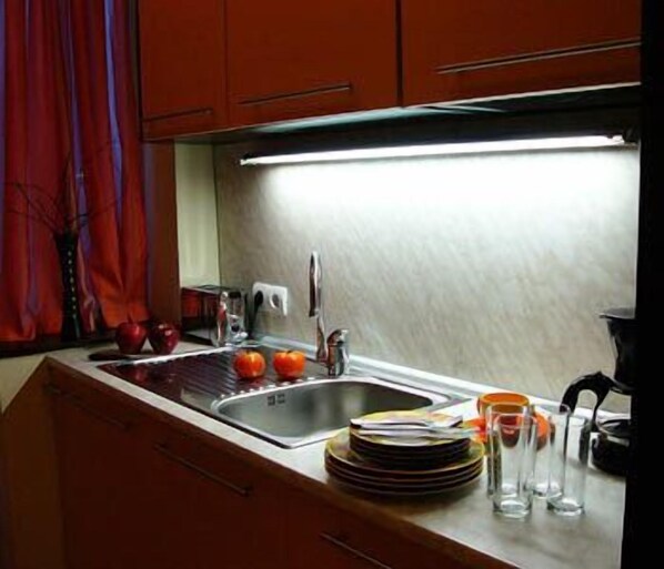 A kitchen with a stainless steel sink, red cabinets, and a bright overhead light. - BIZ Apart Sofia (Sofia)