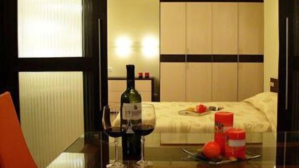 A hotel room with a bed, a bedside table with a bottle and glasses, and a fruit plate. - BIZ Apart Sofia (Sofia)