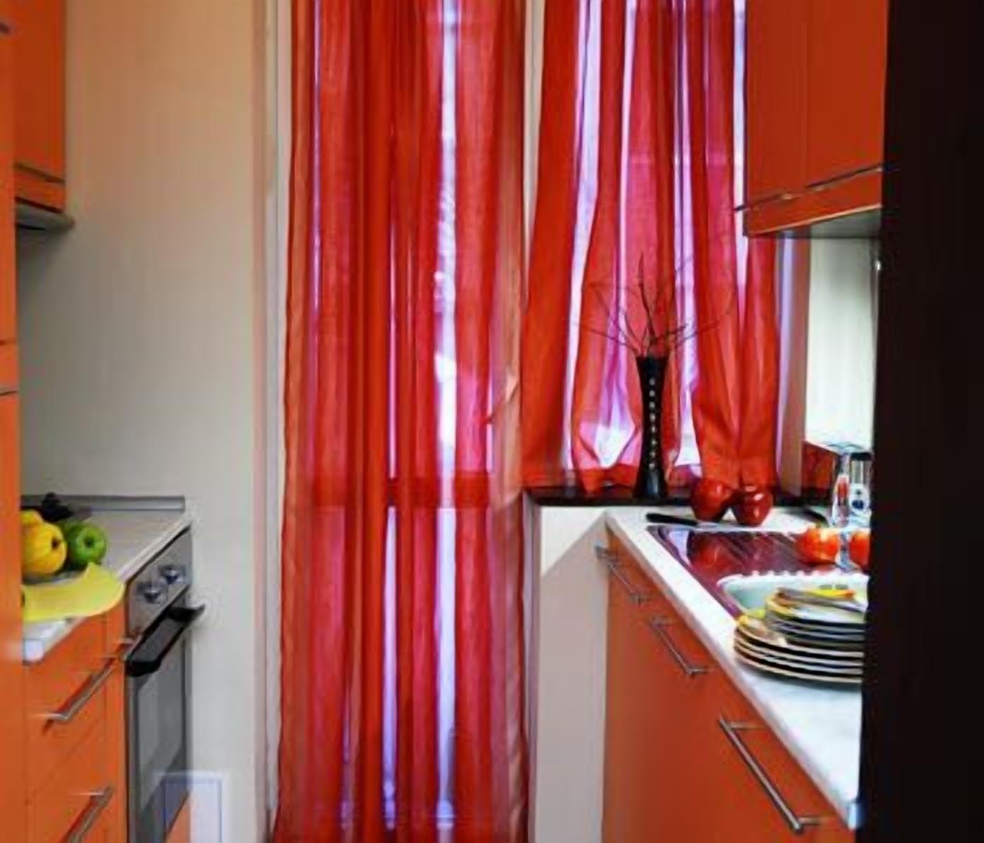 Une cuisine avec des rideaux rouges, une cuisinière et un évier rempli de vaisselle.