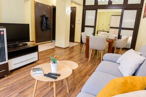 A modern living room with a flat-screen TV, a sofa, a coffee table with remotes, and a dining area with chairs and a table. - BIZ Apart Sofia (Sofia)