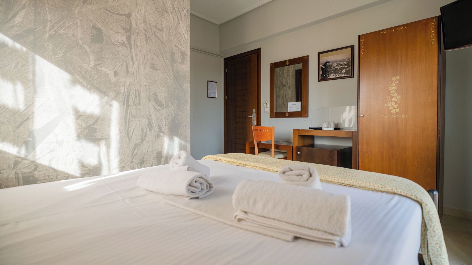 A hotel room with a bed, a desk, a chair, and a wardrobe.