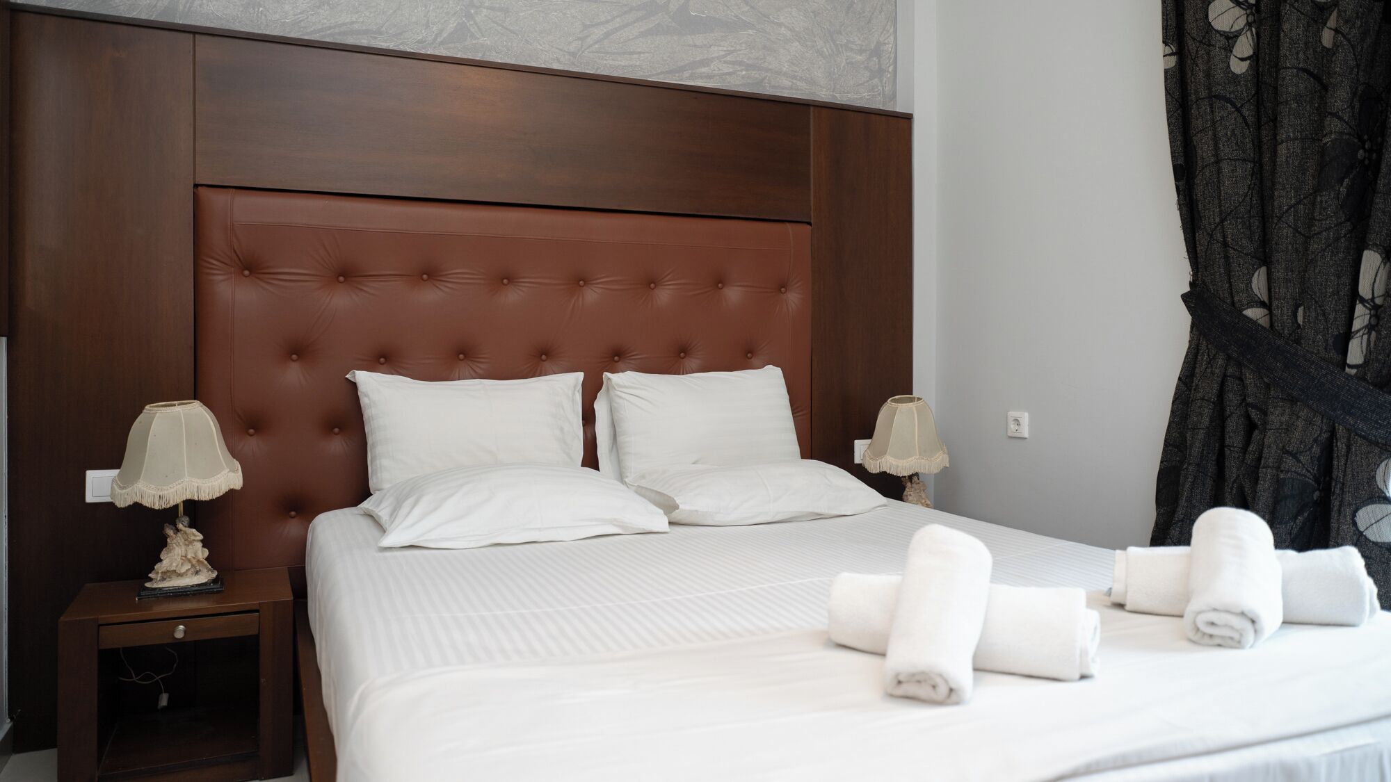 Una cama bien tendida con sábanas y almohadas blancas, un cabecero de madera y dos mesitas de noche con lámparas.