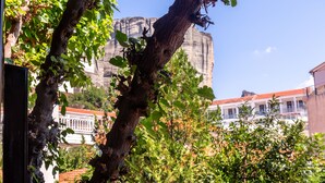 A building with a red-tiled roof, a large rock formation in the background, and a tree in the foreground. - Toti Boutique Rooms  (Kalabaka)