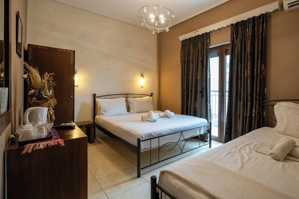A hotel room with two beds, a desk, a mirror, and a chandelier.