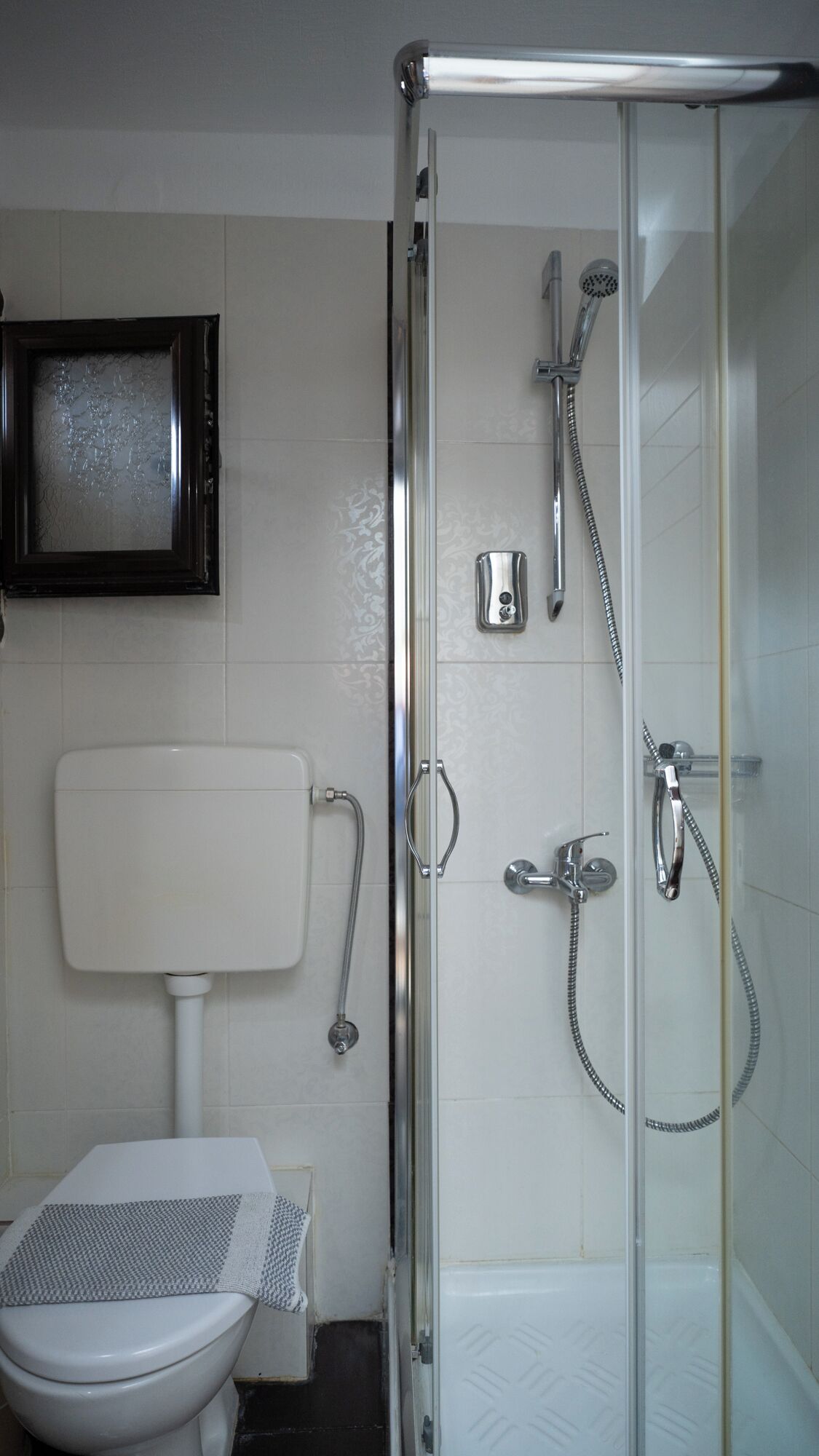 Uma casa de banho com sanita, chuveiro com porta de vidro, lavatório e espelho.