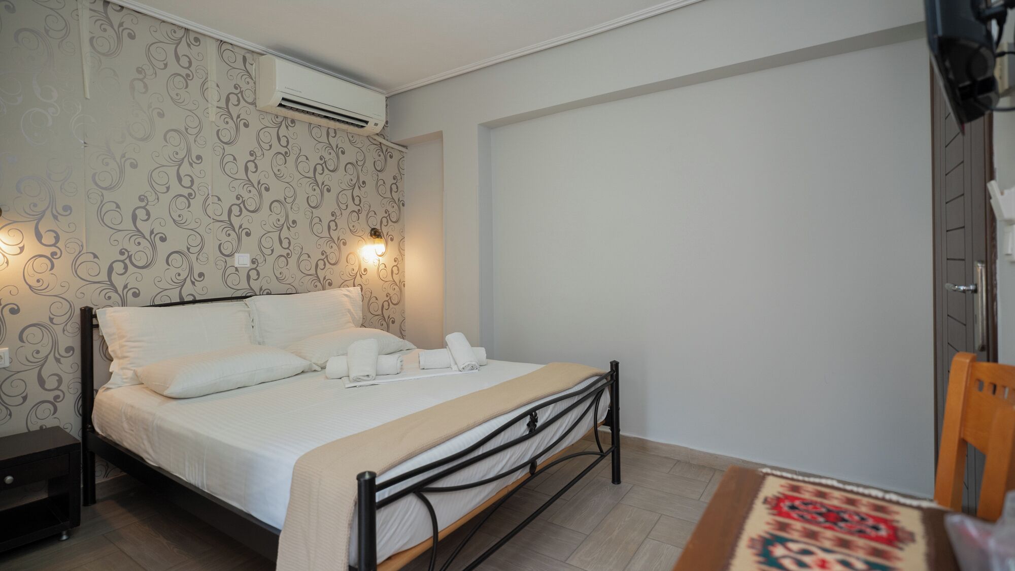 Un dormitorio con cama, mesita de noche, aire acondicionado instalado en la pared y un diseño decorativo en la pared.
