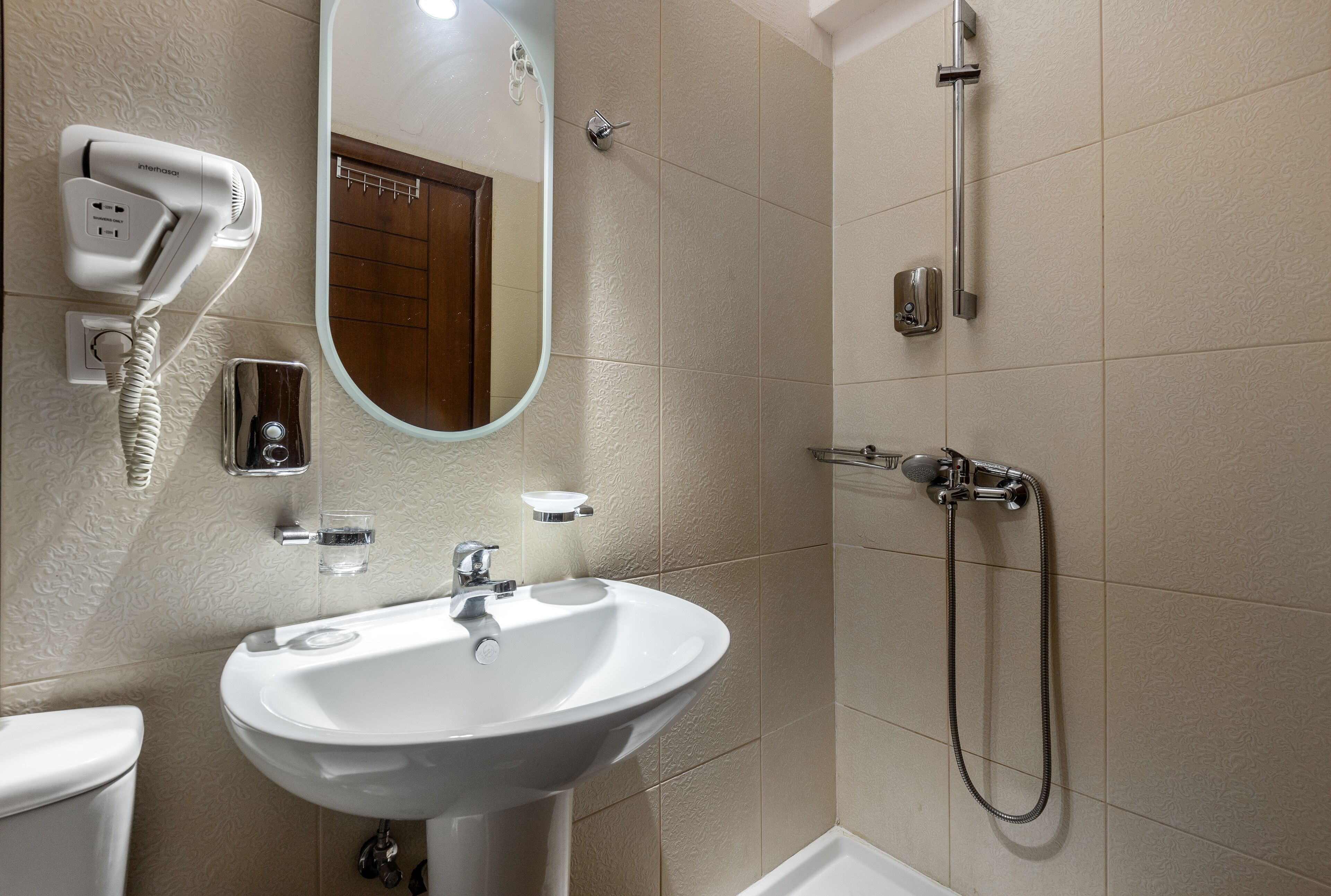 A bathroom with a white sink, a mirror, a hairdryer, and a shower.