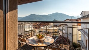 A balcony with a table and chairs, a fruit bowl, and a view of mountains and buildings. - Toti Boutique Rooms  (Kalabaka)