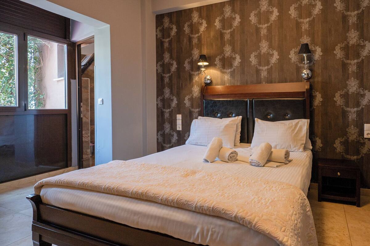 A hotel room with a large bed, two bedside lamps, a wooden headboard, and a chair.