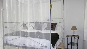 Ein Bett mit Baldachin, ein Nachttisch mit Lampe und ein kleiner runder Tisch ebenfalls mit einer Lampe.