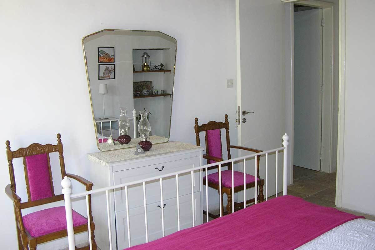 A bedroom with a bed, two chairs, a dresser, a mirror, and a door.