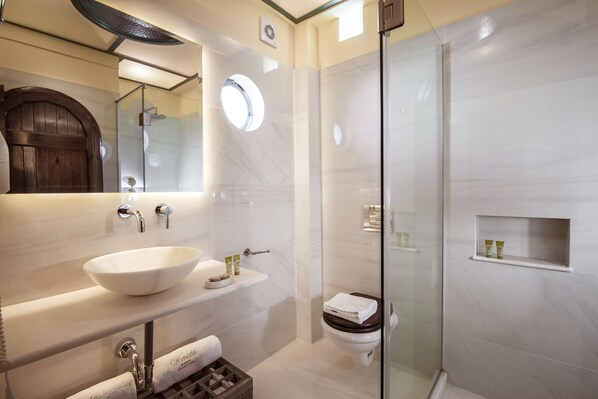 Un baño moderno con un lavamanos grande de color blanco, una ducha con cerramiento de vidrio y un inodoro con asiento de madera.
