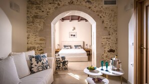 Una habitación acogedora con pared de piedra, una cama con ropa de cama azul y blanca, un sofá blanco con cojines estampados y una pequeña mesa con una jarra y vasos.