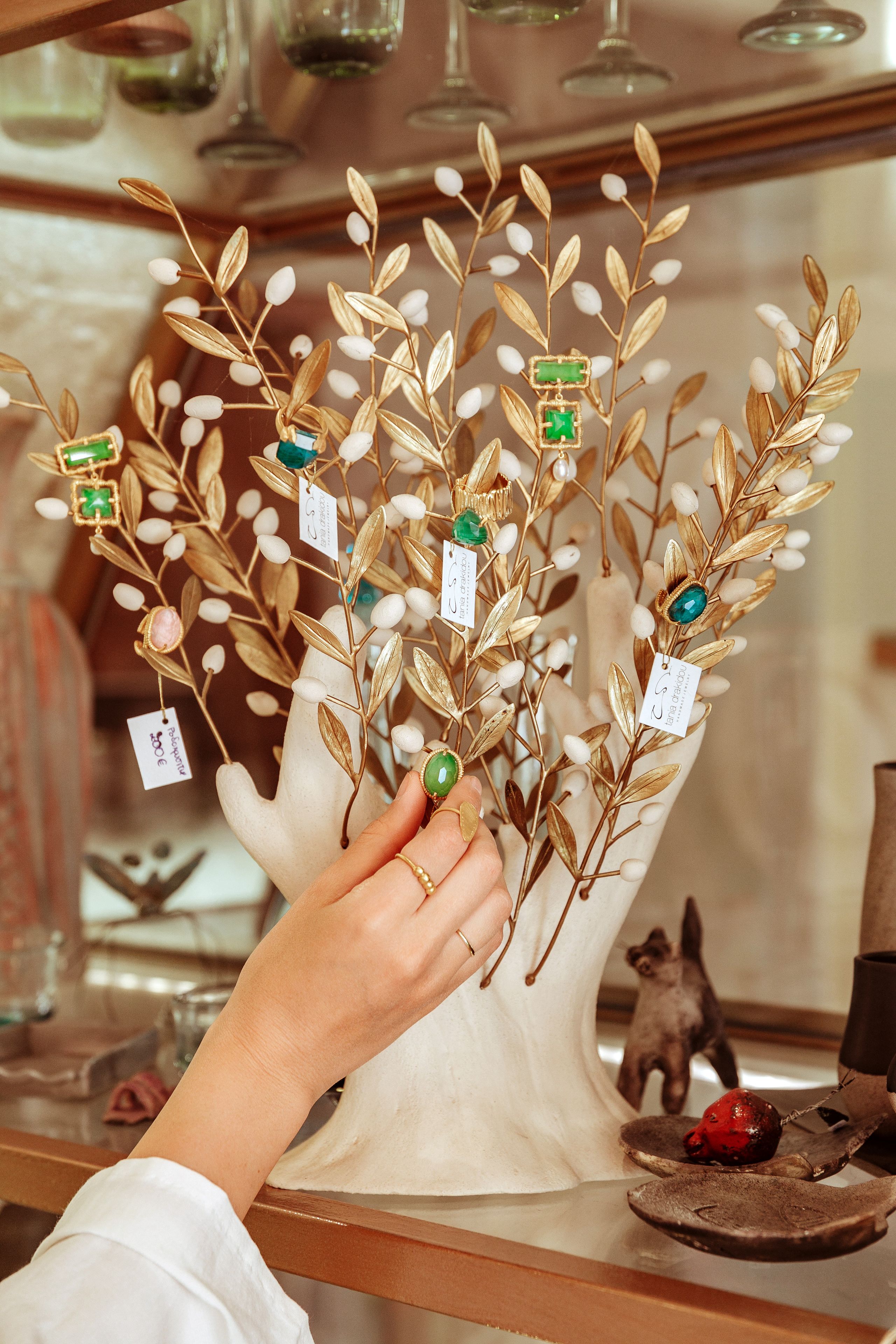 A hand holding a decorative branch with leaves and gemstones, with price tags visible.