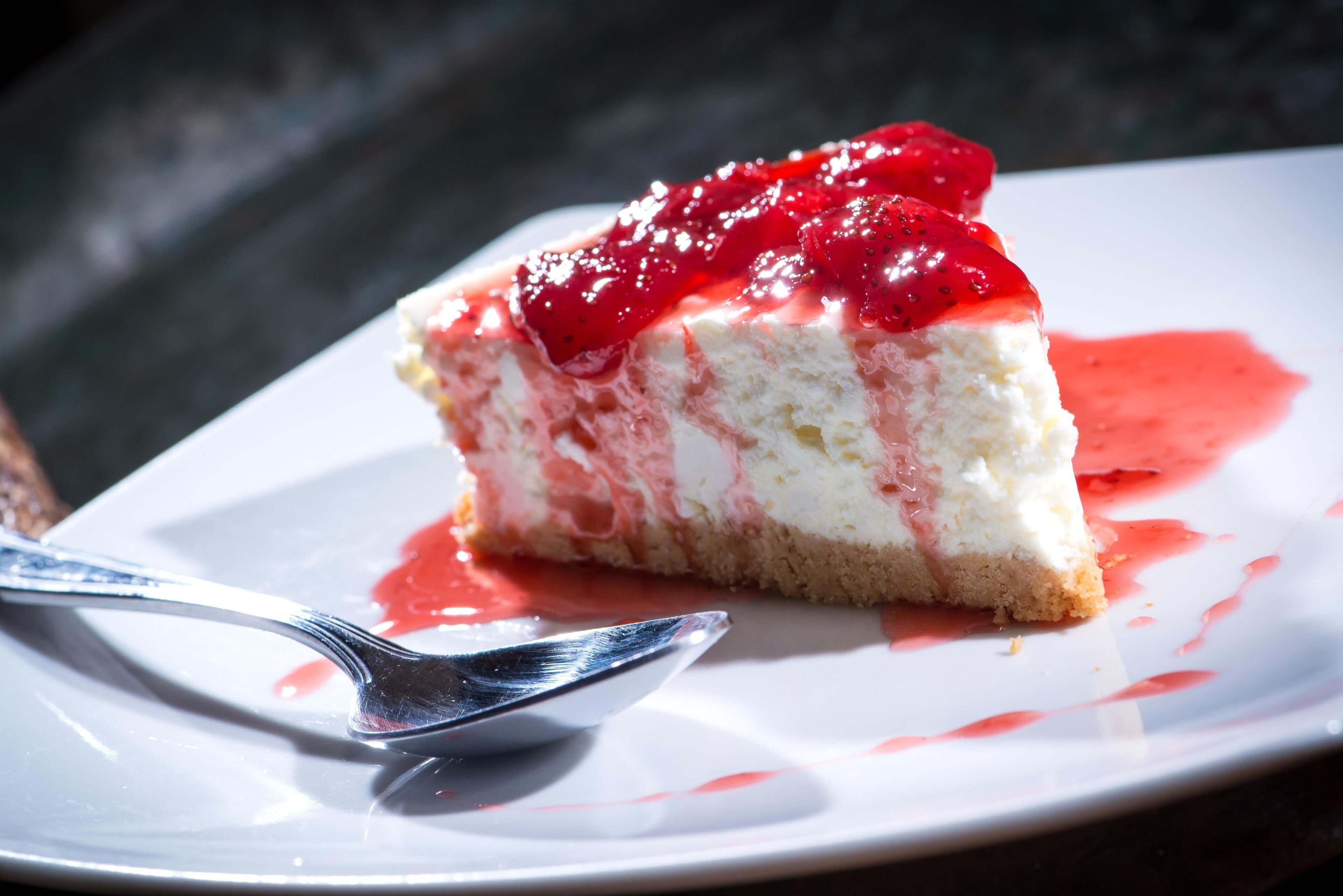 Una porción de pastel de queso con cobertura de fresa sobre un plato blanco.