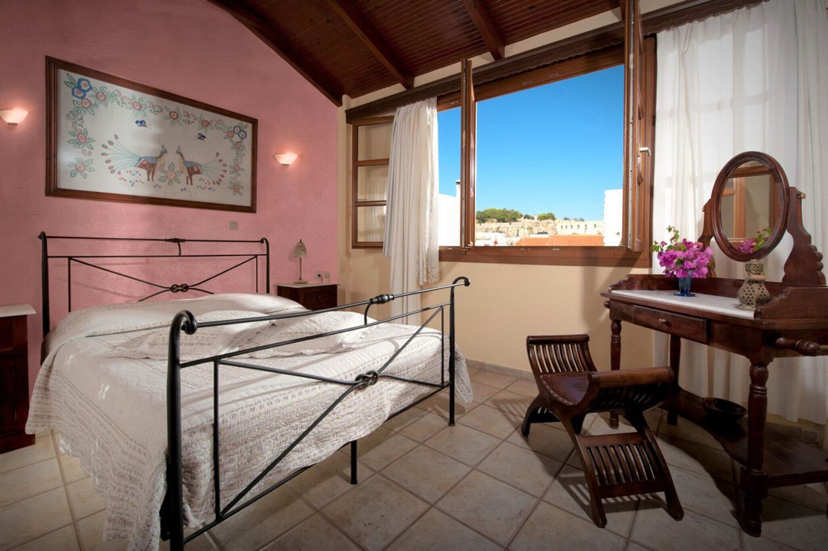 Un dormitorio con cama, escritorio, silla, ventana con vistas y un cuadro en la pared.