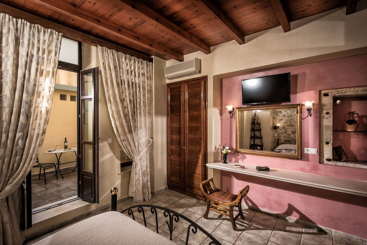 Une chambre avec un plafond en bois, un lit, une chaise, une coiffeuse avec un miroir et un téléviseur fixé au mur.