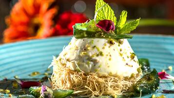 A dessert on a plate with a blue rim, garnished with mint leaves and a rose petal, surrounded by scattered nuts and a green leaf.