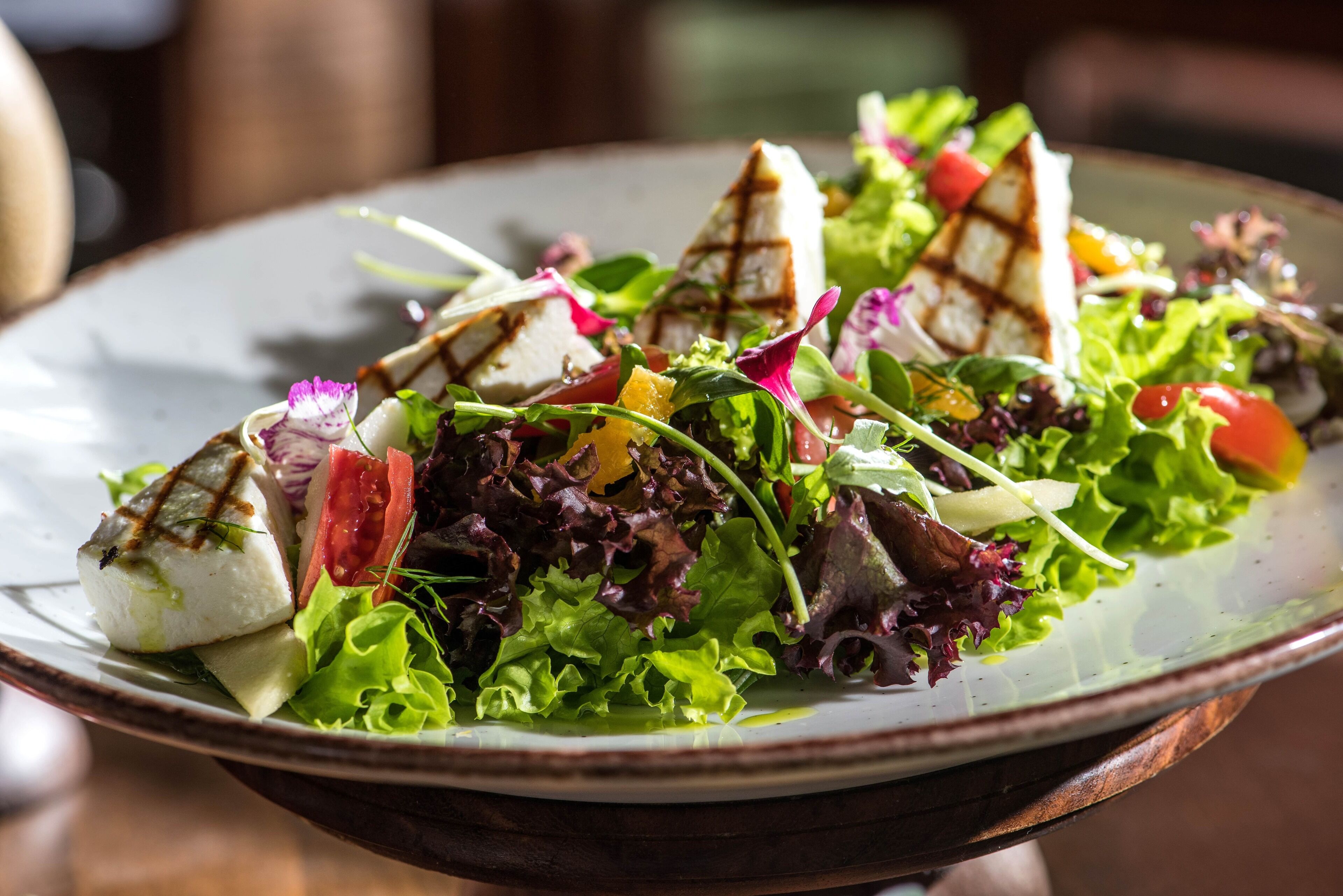 A plate of salad with various greens, tomatoes, and grilled cheese.