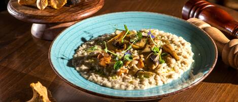 A plate of risotto with mushrooms and herbs, a wooden board with truffles, and a pepper grinder on a wooden table.