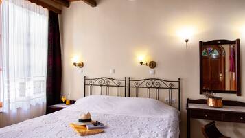 Una cama bien tendida con una colcha blanca, cabecera de madera y dos lámparas fijadas a la pared.