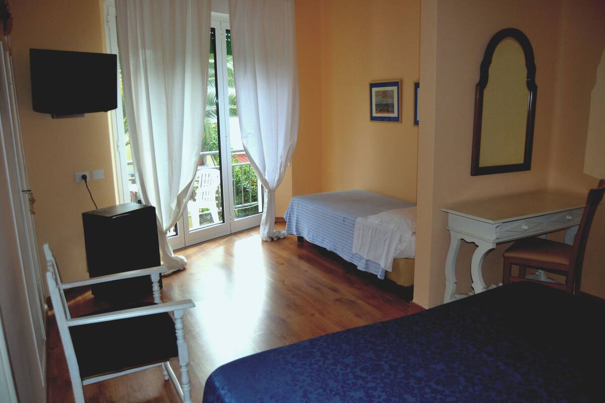 A bedroom with a bed, a desk, a chair, a television, and a window with curtains.