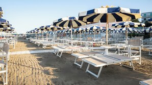 A beach with rows of white sun loungers and striped beach umbrellas. - Ausonia (Follonica)
