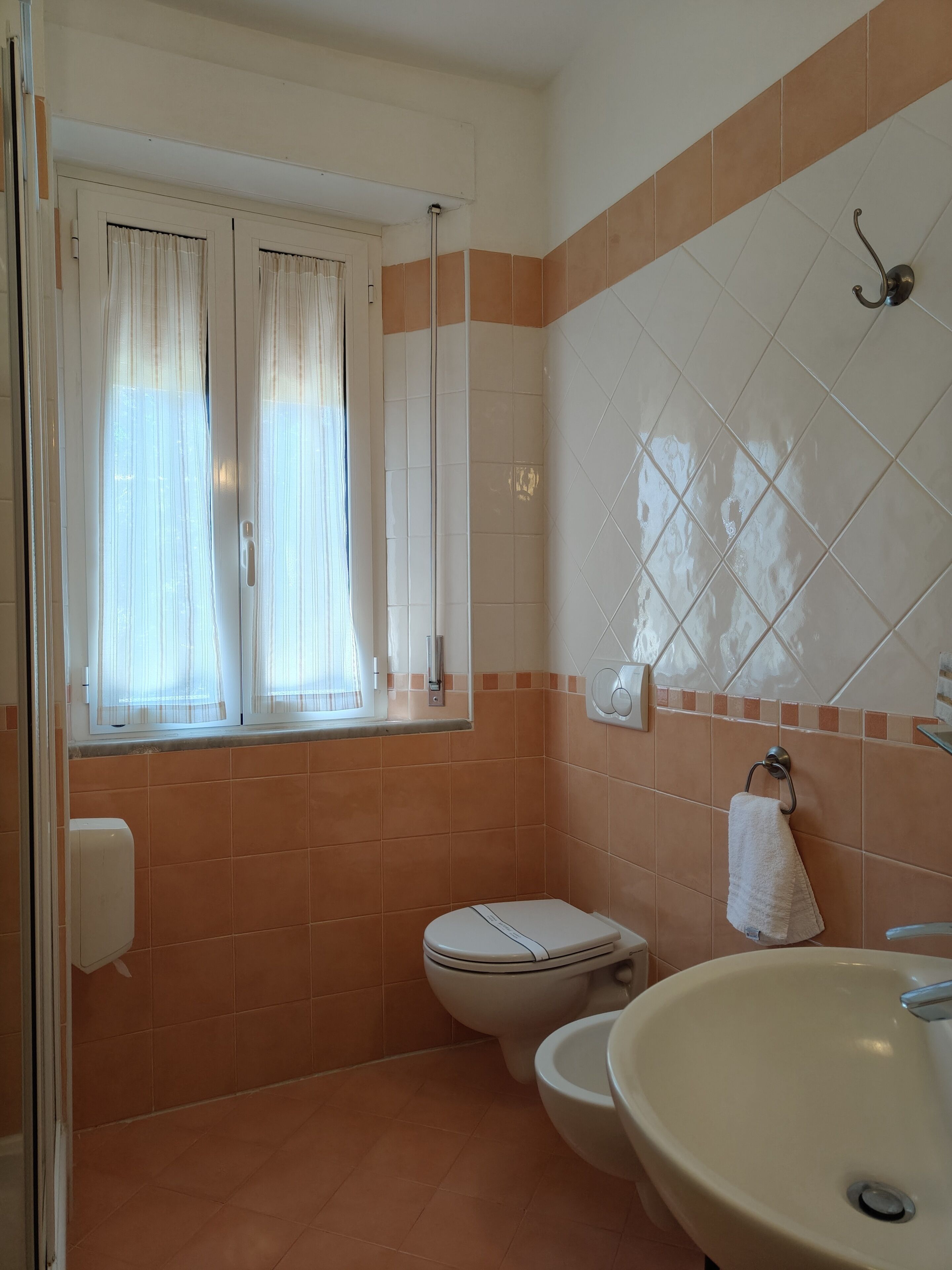 Un baño con inodoro, lavamanos y ventana con cortinas.