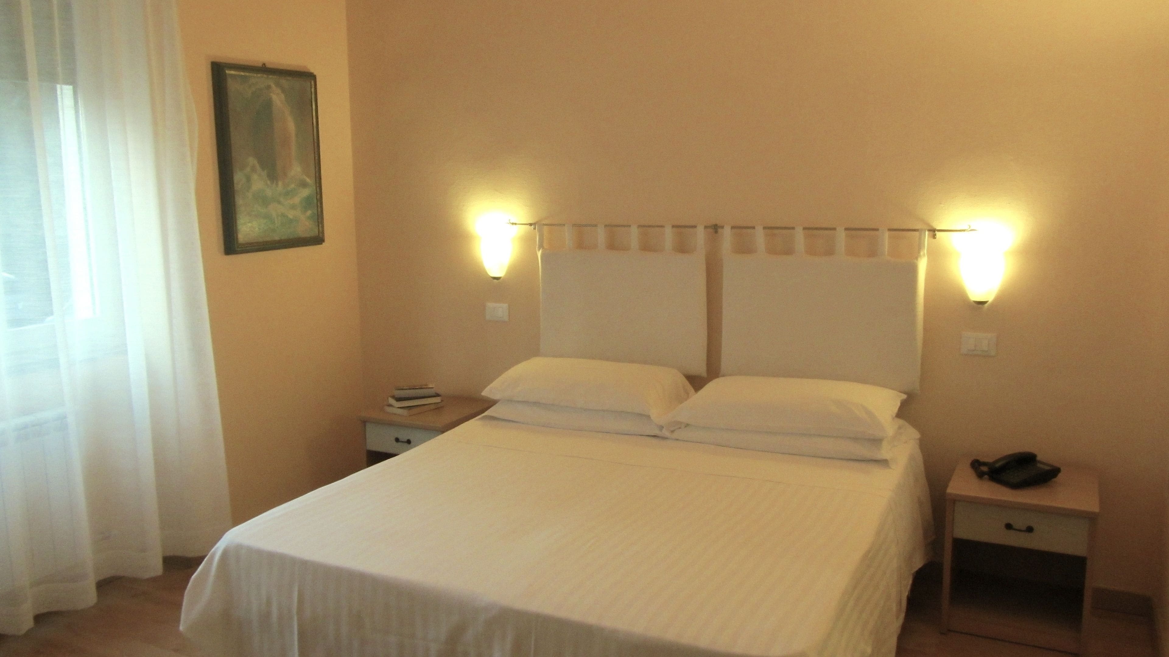 A neatly made bed with white linens, two bedside tables with lamps, and a painting on the wall.