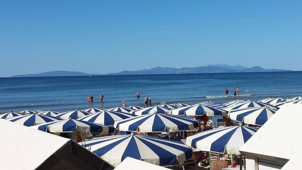 A beach with rows of striped beach umbrellas and people swimming in the water. - Ausonia (Follonica)