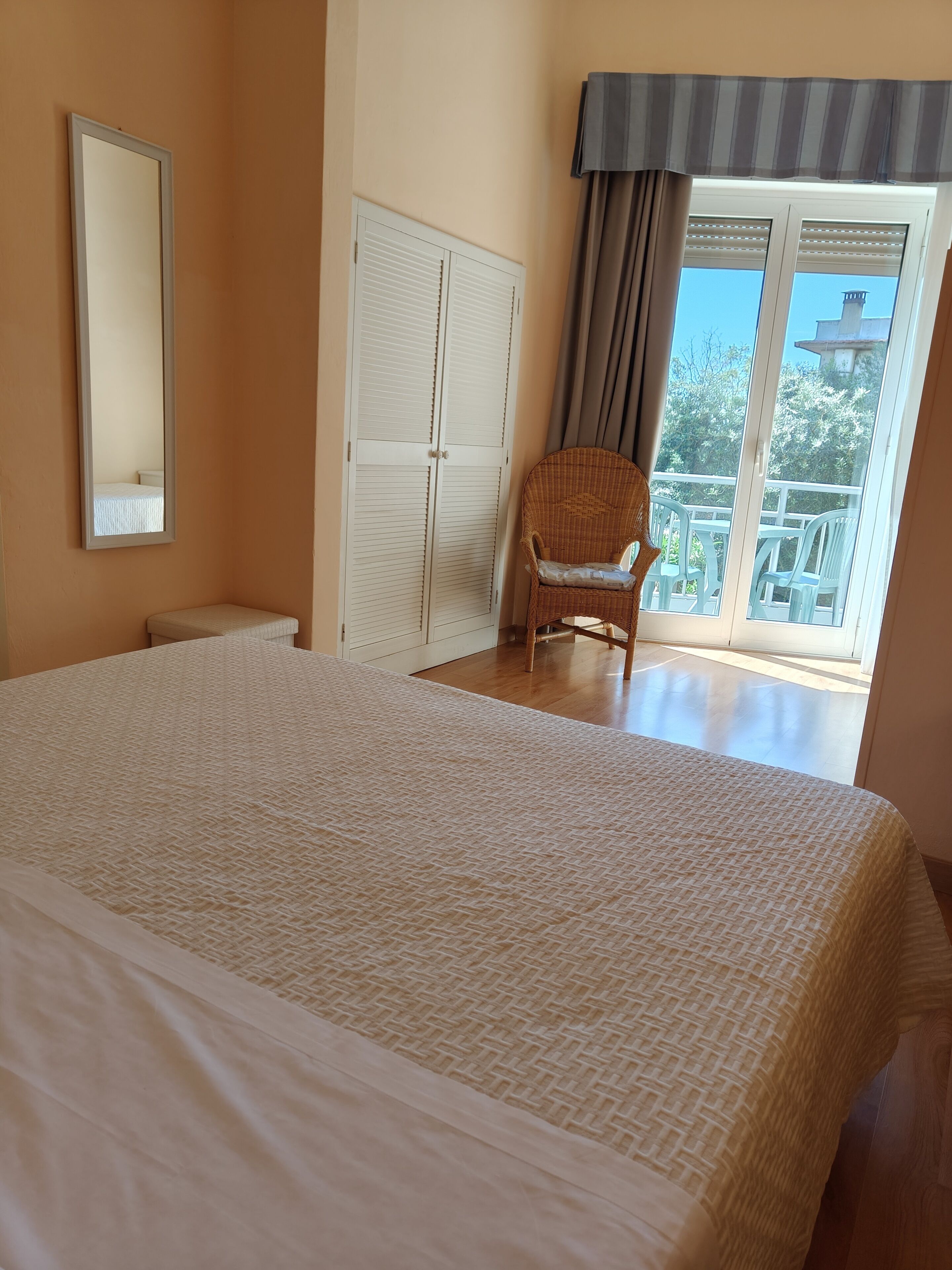 Ein Schlafzimmer mit einem großen Bett, einem Sessel, einem Kleiderschrank und einem Balkon mit Aussicht.