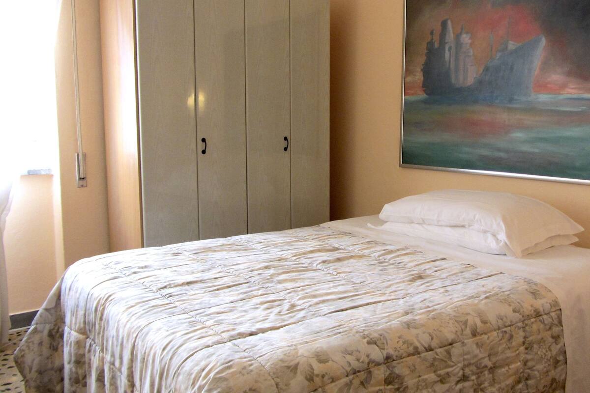 A hotel room with a bed, a wardrobe, and a painting on the wall.
