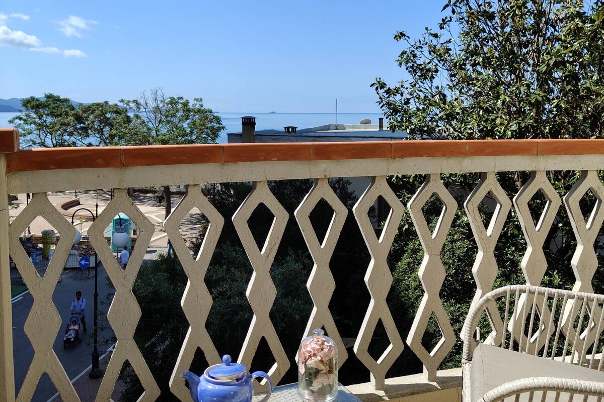 A balcony with a table set for tea, a chair, and a view of the sea.