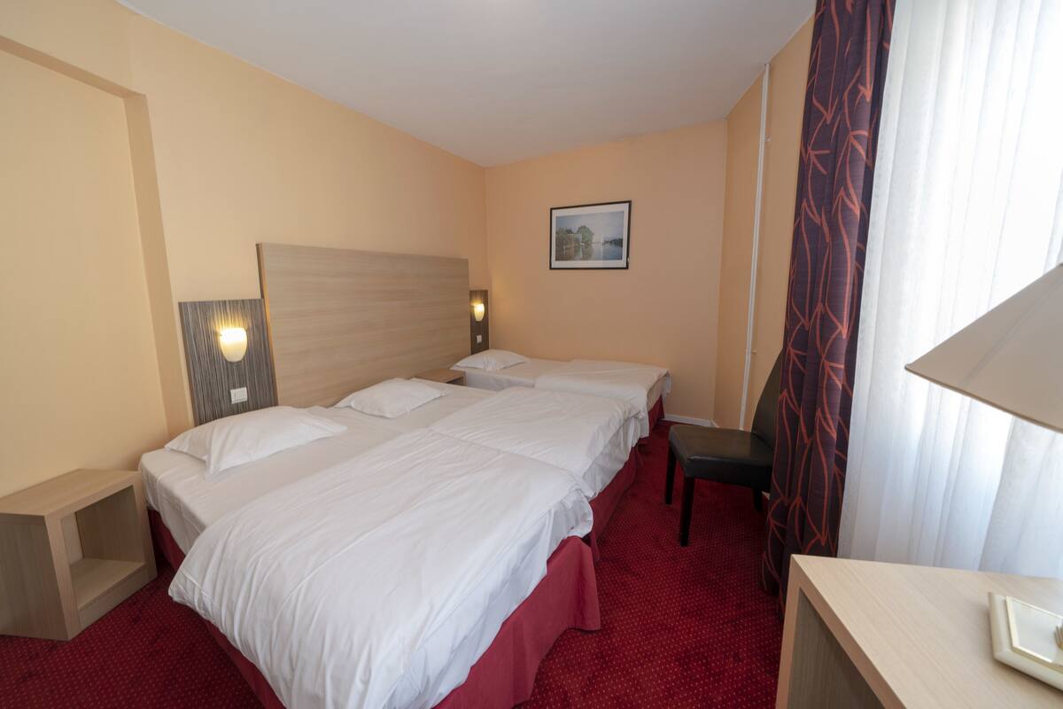 Une chambre d’hôtel avec deux lits, un bureau, une chaise, une table de chevet, une lampe et un tableau au mur.